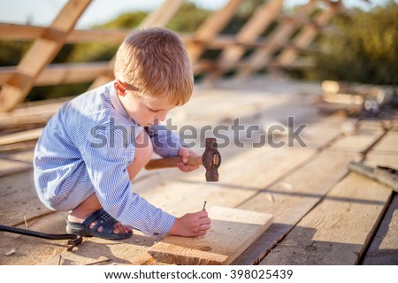 Child (boy) hammers nails with a hammer  in a wooden board on the roof