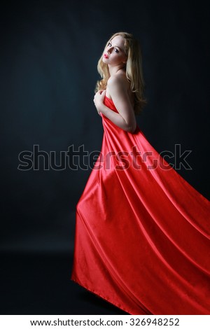 Beautiful blonde woman in long flowing red silk dress. Dark background.