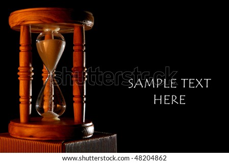Vintage wood hourglass with warm light, isolated on black. Free space for custom text on the right