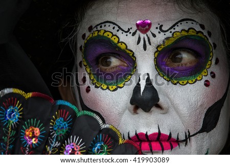 Attractive woman with colorful skull makeup and hand fan. Mexican Day of the dead Catrina woman wearing skull makeup for spooky celebration.