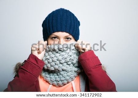 Portrait of a beautiful girl covers her face with a scarf in winter, warm clothing. hipster, on a gray background