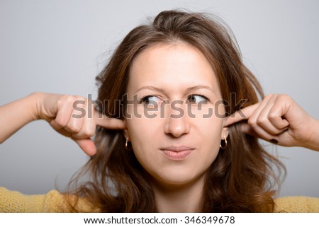 beautiful young girl covers his ears with his hands, studio shot isolated on the gray background