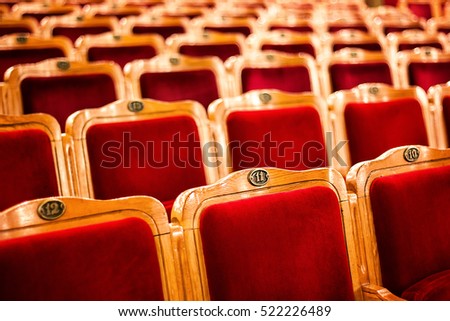 Sets on an empty theatre, taken with selective focus and shallow depth of field. Empty vintage red seats with numbers, teather chair, cinema seats. Movie theater auditorium with lines of red chairs.