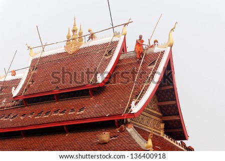 LUANG PRABANG LAOS MARCH 31: Monks work to resurface the roof and repaint their pagoda on march 30 2013 in Luang Prabang LAOS Buddhism is the faith of 96% of the Lao population.