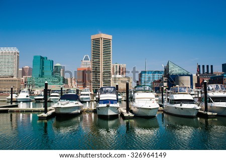 Boats on the water of Baltimore, Maryland\'s Inner Harbor with city buildings in the background against a clear blue sky