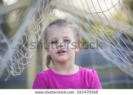 Little girl staying between football net and playing with it