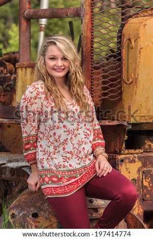 Portrait of a beautiful young woman with long blond hair.  She is outdoors sitting on a tractor.