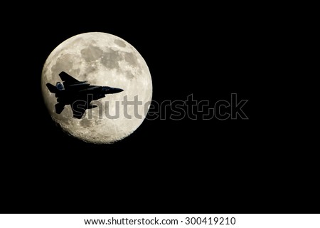 Silhouette of airplane flying in front of moon.