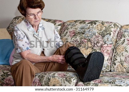Mature lady putting medical boot on broken foot.