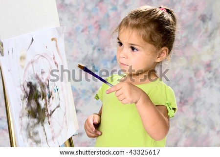 Cute little girl in green blouse playing with water colors on easel.