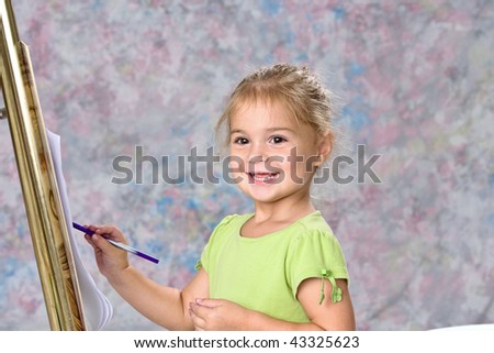 Cute little girl in green blouse playing with water colors on easel.