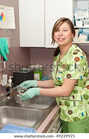 Smiling female medical assistant cleaning medical instruments in sink.
