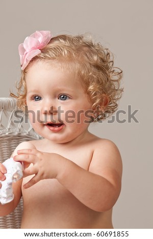 Portrait of one year old baby girl wearing pink bow in hair holding a toy doll.