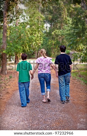 Mother and two sons walking down country road holding hands.