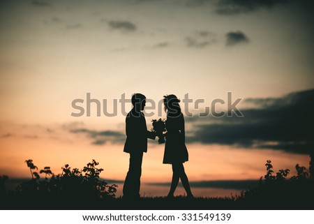 Couple in love silhouette during sunset - A Young couple in love outdoor at the sunset - man gives flowers