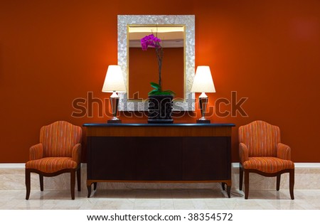 Modern interior with a luxurious dresser with classic lamps, plant and a mirror in a hallway with two classic chairs.