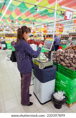 SAMARA, RUSSIA - SEPTEMBER 23, 2014: Young woman weighing vegetables on electronic scales in produce department of the Magnit store. Russia\'s largest retailer