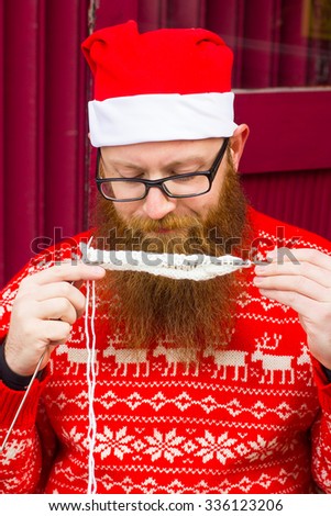 A bearded man in a Christmas hat knits. Handmade Santa Claus, red sweater, jacket, warm clothes, a red beard, festive mood, new year, christmas concept
