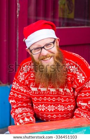 A bearded man in a Christmas hat knits. Santa Claus,red beard red sweater, smile and happy; warm clothes, festive mood, new year, christmas concept