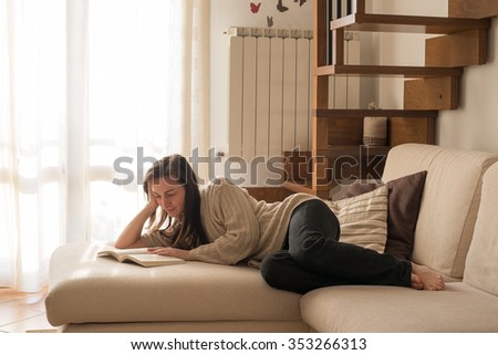 Young woman reading a book on white couch in a cozy living room