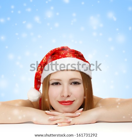 Beautiful young woman in santa claus hat laying on the table on blue background with falling snowflakes