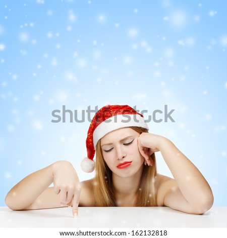 Young woman in santa claus hat posing with wearied look on blue background with falling snow