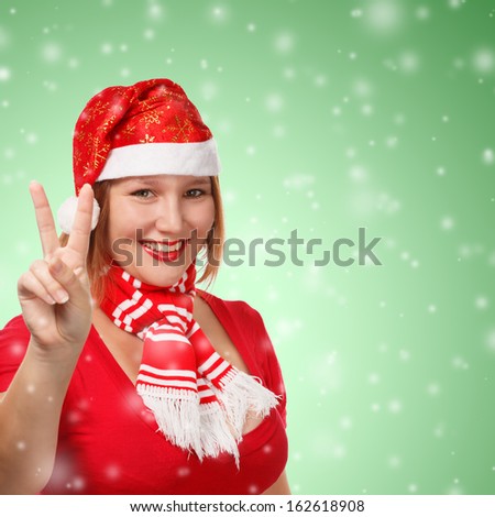 Young woman in new year or christmas suit smiling with victory sign on green background with falling snow