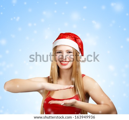Smiling young woman in santa claus hat gesturing like holding something in hands on blue snowfall background