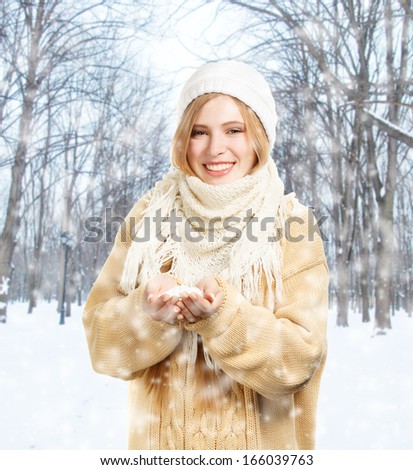 Young smiling woman in warm winter clothing standing with snow in hands in park