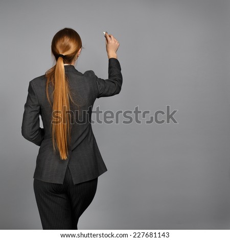 Young beautiful woman in business suit writing with chalk on grey background. Back view.