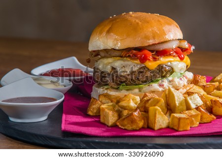 Big burger served for eating. Burger contains lots of extras cheese, bacon, onion, ketchup, lettuce, mayonnaise.