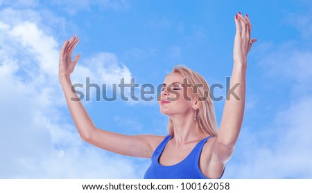 Pretty young woman with arms raised and closed eyes standing on sky background