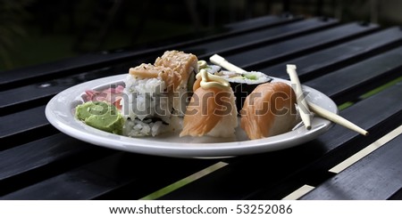 a plate of sishi on a white plate lying on a black wood table with eating utensils
