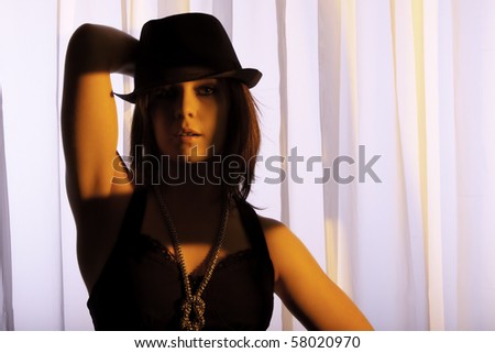 beautiful young Caucasian woman with red hat wearing a black top and top hat against a curtain in warm sunset light