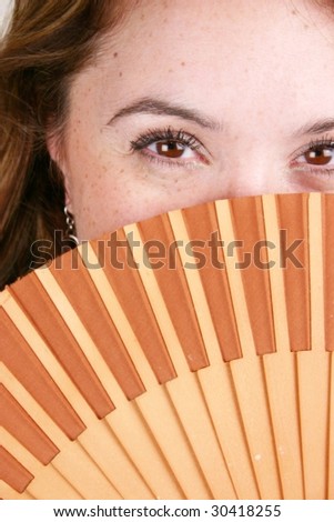 Brunette Spanish woman with brown eyes holds a wooden folding fan over her face