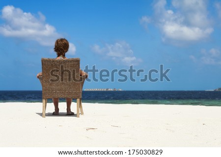 a woman sitting looking at the sea, seen from behind