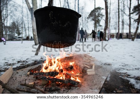 Tourist pot hanging over the fire in the forest in winter, cooking over a campfire