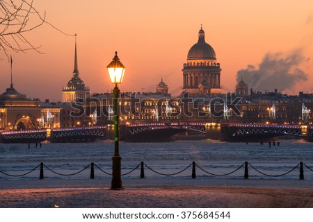 View of the evening city decorated with lights. In the foreground a street light. In the background, the main attractions - the Palace Bridge and St. Isaac sobo. Russia, Saint-Petersburg.