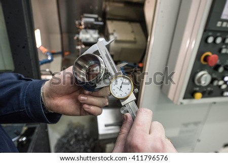 Turner miller verifies the accuracy of manufacturing steel parts with a special caliper Additional scale - the size of the measurement device. In the background to blur milling machine.
