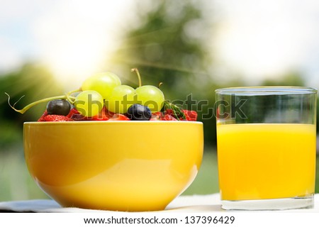 glass of orange juice and bowl of fresh berries in an outdoor setting - a healthy breakfast in the garden.