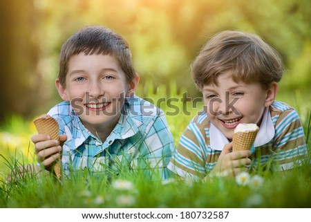 Happy smiling boys eat ice cream on a grass outdoors in spring park