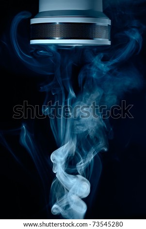 Macro view of wispy smoke around white fire sensor or smoke detector, dark background.