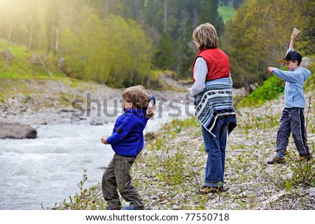 woman with two children gathering and throwing rocks at the river