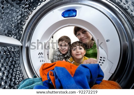 Funny boys and mother loading clothes to washing machine. View from the inside of washing machine.