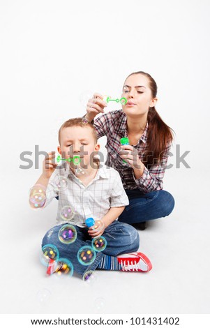 A little boy and a pretty woman sit cross-legged on the floor and let go soap bubbles.