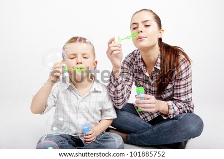 A boy and a woman sit cross-legged on the floor and let go soap bubbles.