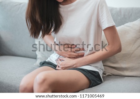 Healthcare medical or daily life concept : Close up stomach of young lady have a stomachache or menstruation pain sitting on a sofa.