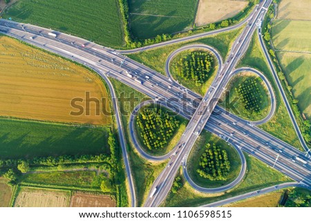 Cloverleaf interchange seen from above. Aerial view of highway road junction in the countryside with trees and cultivated fields. Bird\'s eye view.