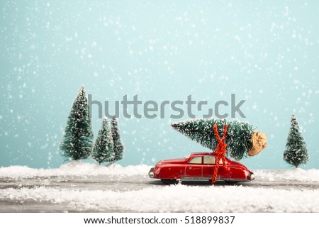 Red car carrying a Christmas tree in a snowy landscape. Space for text.