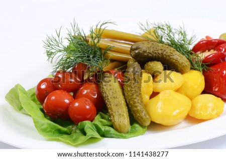 Different types of vegetables on white plate. Pickled cucumbers, tomato cherry, greens, mushrooms and garlic with onion and lettuce served on white plate.